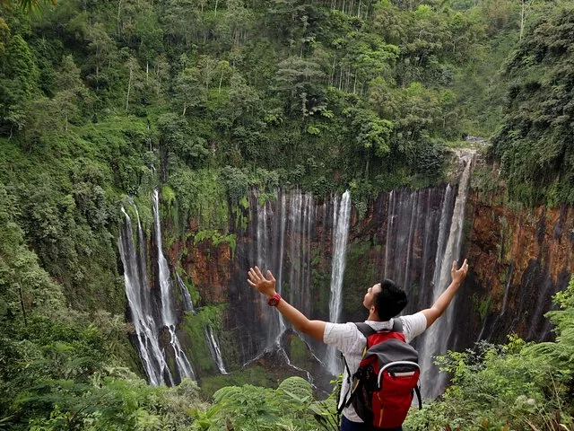 man with a backpack raising his arms at the Tumpak Sewu Waterfall viewpoint