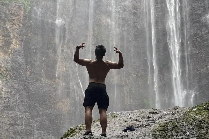 man flexing his muscles with his back turned towards Tumpak Sewu Waterfall