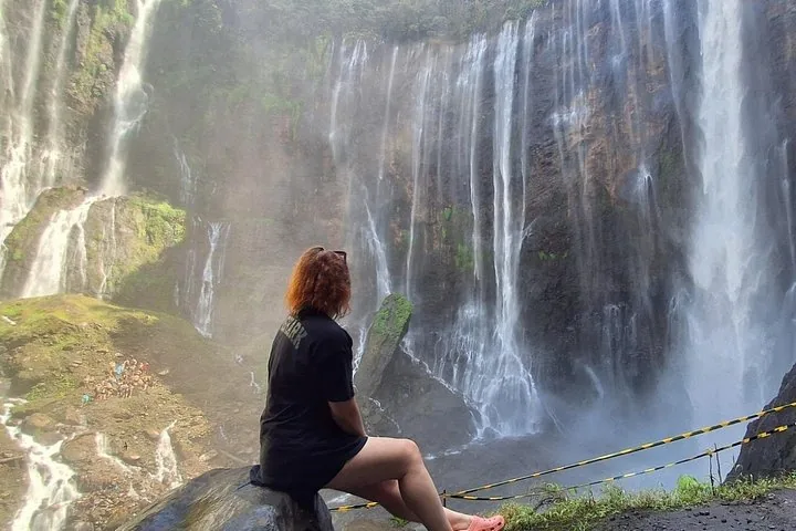 woman sitting on a rock admiring the misty Tumpak Sewu Waterfall